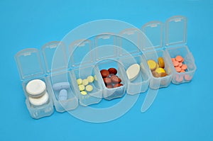 Plastic daily organizer for pills with different pills on blue background with copyspace, top view