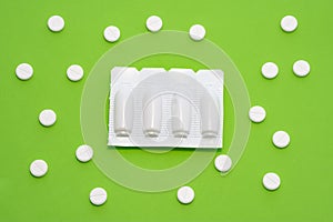 Plastic packaging with vaginal or rectal suppositories is on green background surrounded by round tablets that form ornament in po