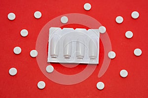 Plastic packaging with vaginal or rectal suppositories is on redbackground surrounded by round tablets that form ornament in polka photo