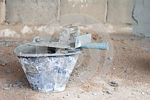 Plastic pail with cement inside and the plastering trowel put on top in the construction site.