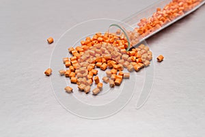 Plastic pallets . Colorant for polymers in granules. Orange granules of raw plastic for industry spilled out of the tube.