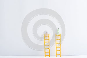 Plastic people figures on ladders on white surface on grey background