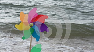 Plastic pinwheel rotates colored with blowing wind stands on sand against the sea with waves.