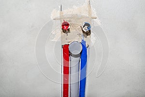 Plastic pipes with hot and cold water coming out of the floor then mounted on the wall, home water system. In the middle a sewage