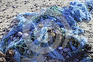 Plastic pollution - blue tangled fishing nets washed up on the b