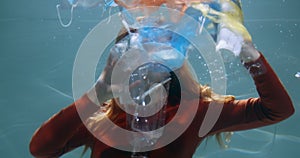 Plastic pollution of the ocean. Young woman spreads single use garbage under water, waste floating around slow motion.