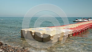 Plastic pontoon cubes floating sea water surface. Seashore with colorful pebbles and clear sea water, sun rays reflecting in water