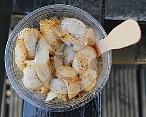 Plastic pot of whelks with vinegar and black pepper and wooden spoon