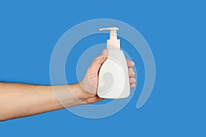 Plastic pump cream bottle and male hand on blue background. Liquid soap bottle. Cosmetic packaging mockup with copy space
