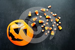 Plastic pumpkin basket with candy corn spilled out. Some of it are broken and look like small teeth. Halloween harmful sweets