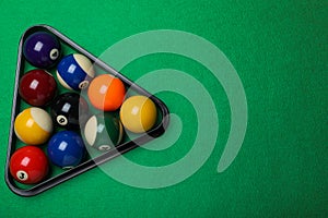 Plastic rack with billiard balls on green table, top view. Space for text