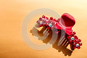 Plastic red hair clip with with rhinestones on the bronze background