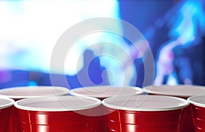 Plastic red party cups in a row in a nightclub full of people dancing on the dance floor in the background.