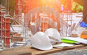 Plastic safety helmet and blueprint on wood and worker construction team working building commercial in site workplace with sunri