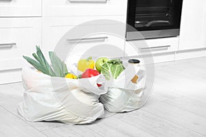 Plastic shopping bags full of vegetables and  on floor in kitchen. Space for text