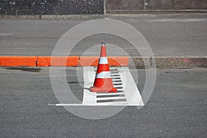 Plastic signaling traffic cone encloses a place in the parking lot for cars.