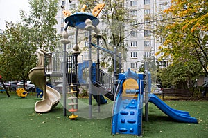 A plastic slide of bright blue and green color against a background of green trees and residential buildings