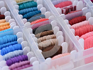 Plastic sorting box full of bobbins with different color embroidery threads.