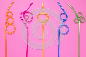 Plastic spiral multicolor tubes on pink paper card. Abstract colorful background of curved cocktail straws. Laconic design. Concep
