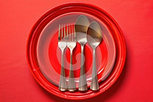 a plastic spoon, fork, and knife arranged neatly on a red plastic plate