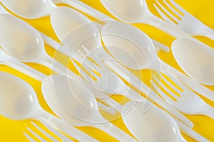 Plastic spoons and forks on yellow background
