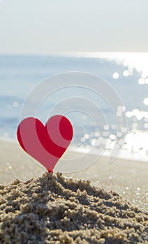 Plastic stick in shape of red heart in sand on sandy beach of sea shore