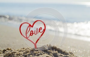 Plastic stick in shape of red heart and word Love in sand on beach seashore