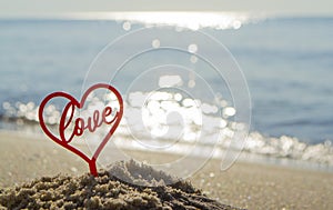 Plastic stick in shape of red heart and word Love in sand on beach seashore