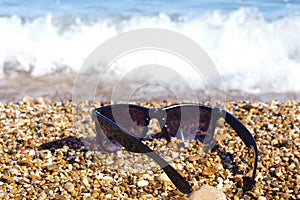 Plastic sunglasses against the background of sea stones. Sea in the background