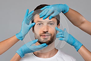 Plastic surgeon hands in protective gloves touching middle-aged man face