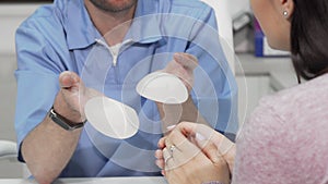 Plastic surgeon showing two breast implants to female patient