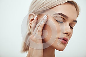 Plastic surgery. Beautiful young blonde woman keeping eyes closed and touching her face with sketch on it