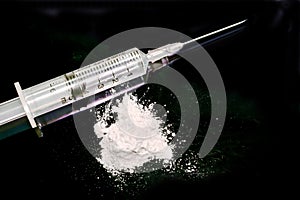 Plastic syringe put in a medical needle and white powder isolate on black background.