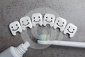 Plastic teeth with cute faces, toothpaste and brush on grey background, flat lay