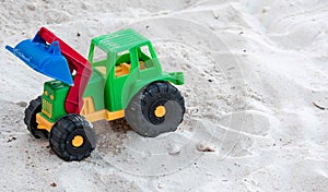 A plastic toy bulldozer color green, red, yellow and blue with black big wheels placed on a white sand in a beach resort