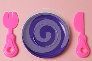 Plastic toys tableware plate, fork, knife on pink background