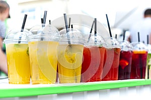 Plastic transparent glasses with different kinds of cold lemonade (yellow, red, green) stays on white table with green