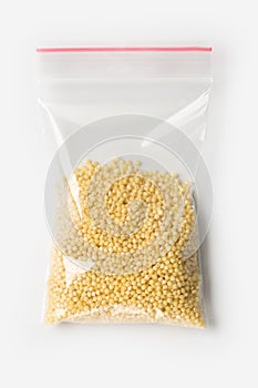 Plastic transparent zipper bag with half raw millet groats isolated on white, Vacuum package mockup with red clip. Concept