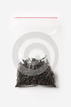 Plastic transparent zipper bag with a little black tea isolated on white, Vacuum package mockup with red clip. Concept.