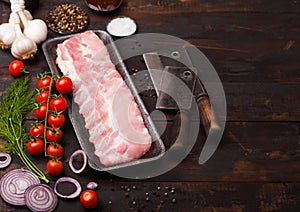 Plastic tray with raw pork ribs and vintage hatchets on wooden background. Fresh tomatoes and red onion with garlic salt and