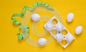 Plastic tray with white eggs and a ruler on a yellow pastel background, minimalism trend, top view.