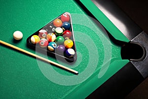 Plastic triangle rack with billiard balls and cue on green table, above view