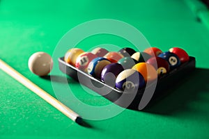 Plastic triangle rack with billiard balls and cue on green table, closeup