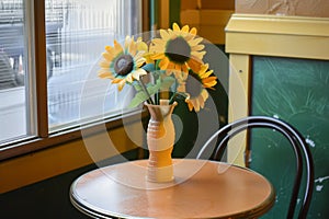 a plastic vase with faux sunflowers on a small bistro table in a caf corner photo
