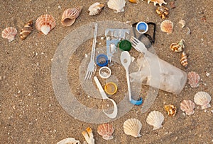 Plastic waste: bags, disposable plastic appliances, plastic lids on the sand in a shell frame. Concept of ecology, environmental