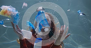 PLASTIC WASTE. Cinematic shot of young woman spreading trash bags and bottles under water floating around slow motion.