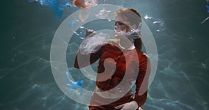 Plastic waste problem. Cinematic slow motion view of young woman look at garbage bags and bottles floating under water.