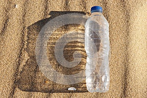 A plastic water bottle lies on the sand casting a wide shadow, the concept of plastic pollution