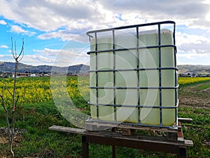 Plastic water tank in a farm field under a blue cloudy sky and sunlight