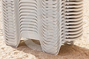 Plastic white chaise lounges stacked in a pile on the beach, close-up, concept of leisure